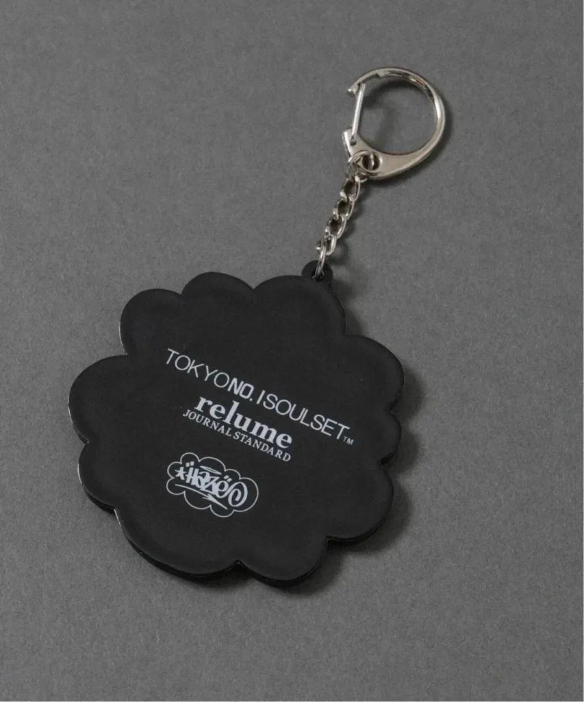Black scalloped keychain with silver clasp and chain, printed with “TOKYO NO SOULSET relume” on gray fabric surface