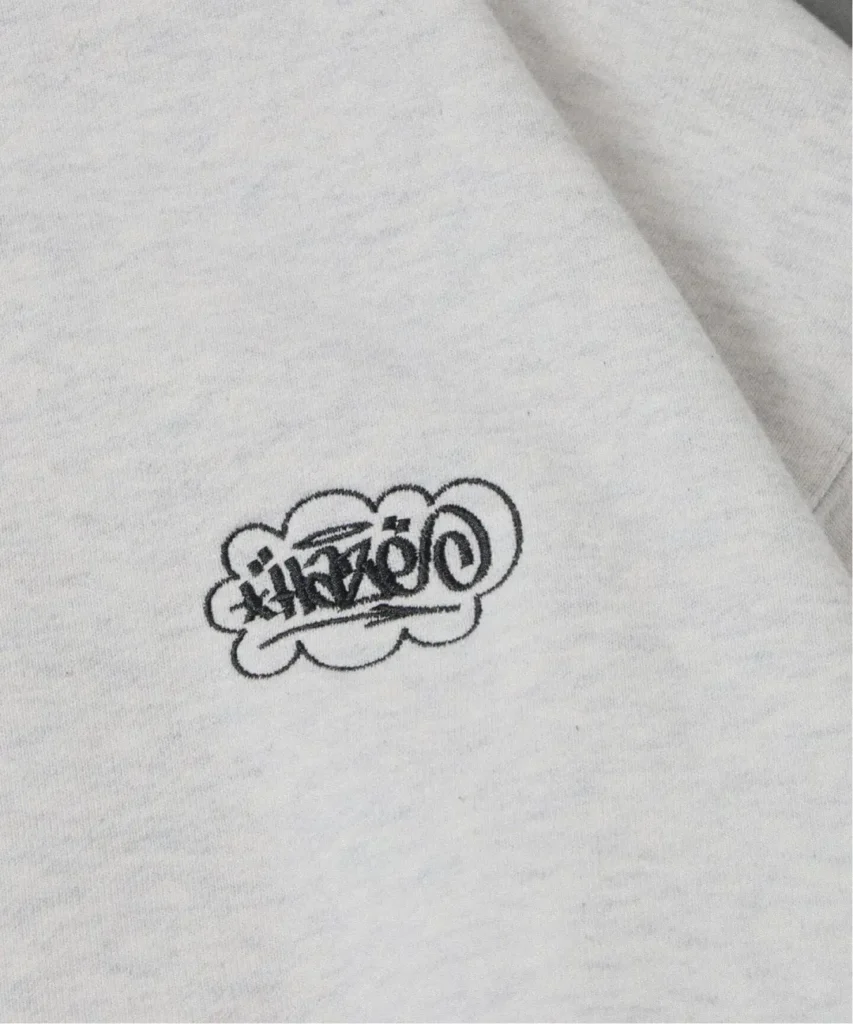 Close-up of white fabric featuring a small black outlined cloud graphic with stylized lettering