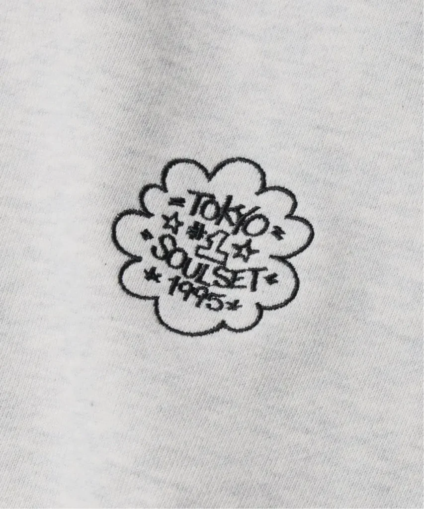Embroidery on white fabric reads “TOKO OUTLET 1995” inside a scalloped flower shape