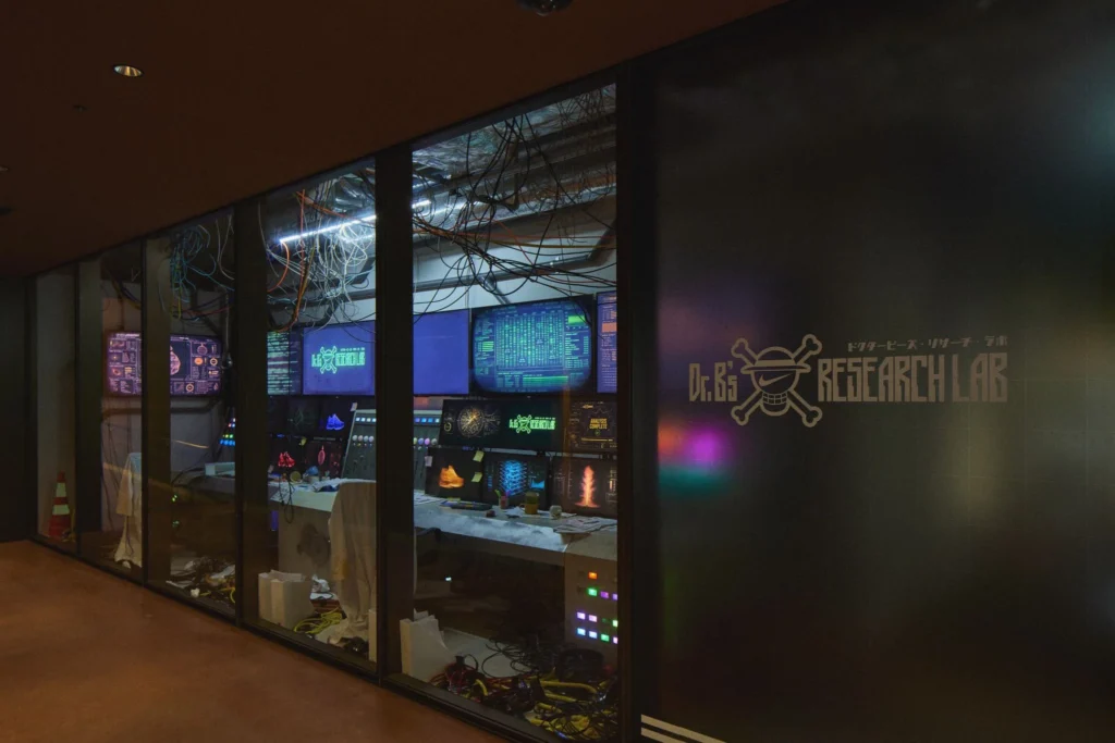 Glass-walled arcade laboratory with glowing monitors, cables, and “RESEARCH LAB” lettering on the door