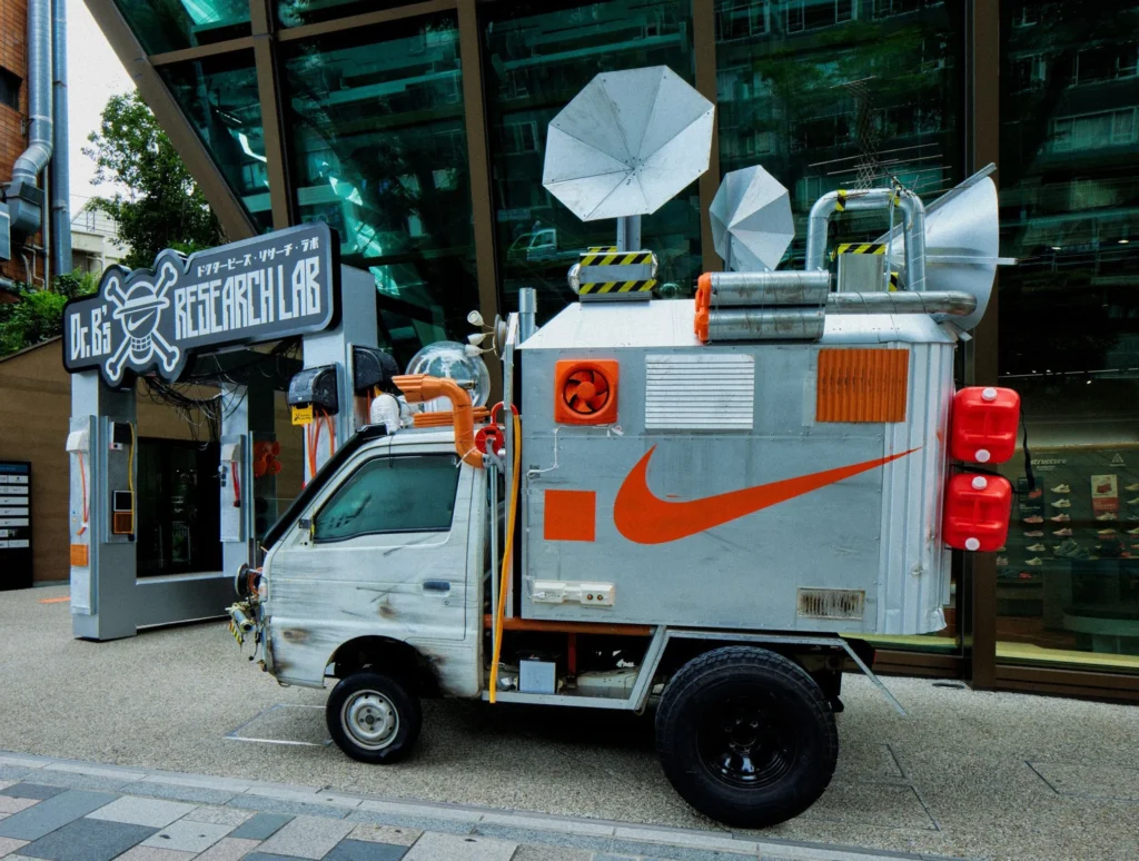 Silver food truck with large Nike swoosh, rooftop equipment, and Japanese storefront sign parked on a city sidewalk