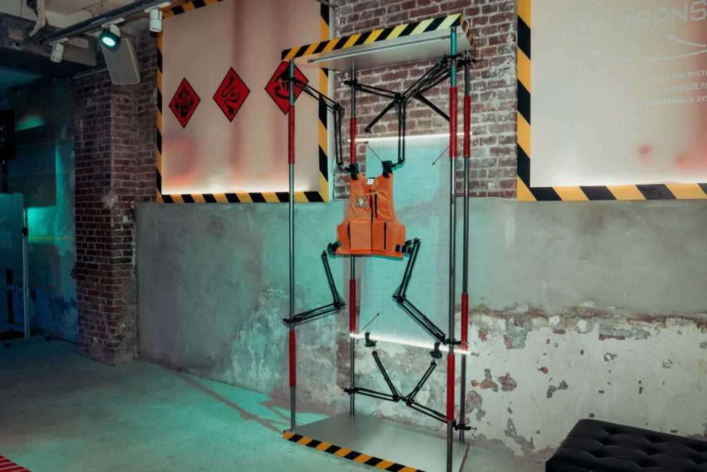 Orange mannequin strapped into a black metal frame in an industrial brick-walled room with hazard stripes
