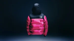 Pink-and-black North Face puffer jacket with hood, suspended against a dark blue background