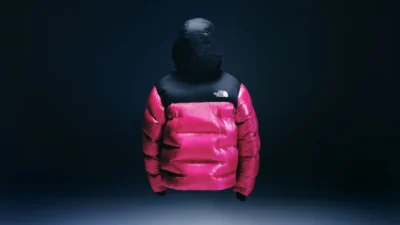 Pink-and-black North Face puffer jacket with hood, suspended against a dark blue background