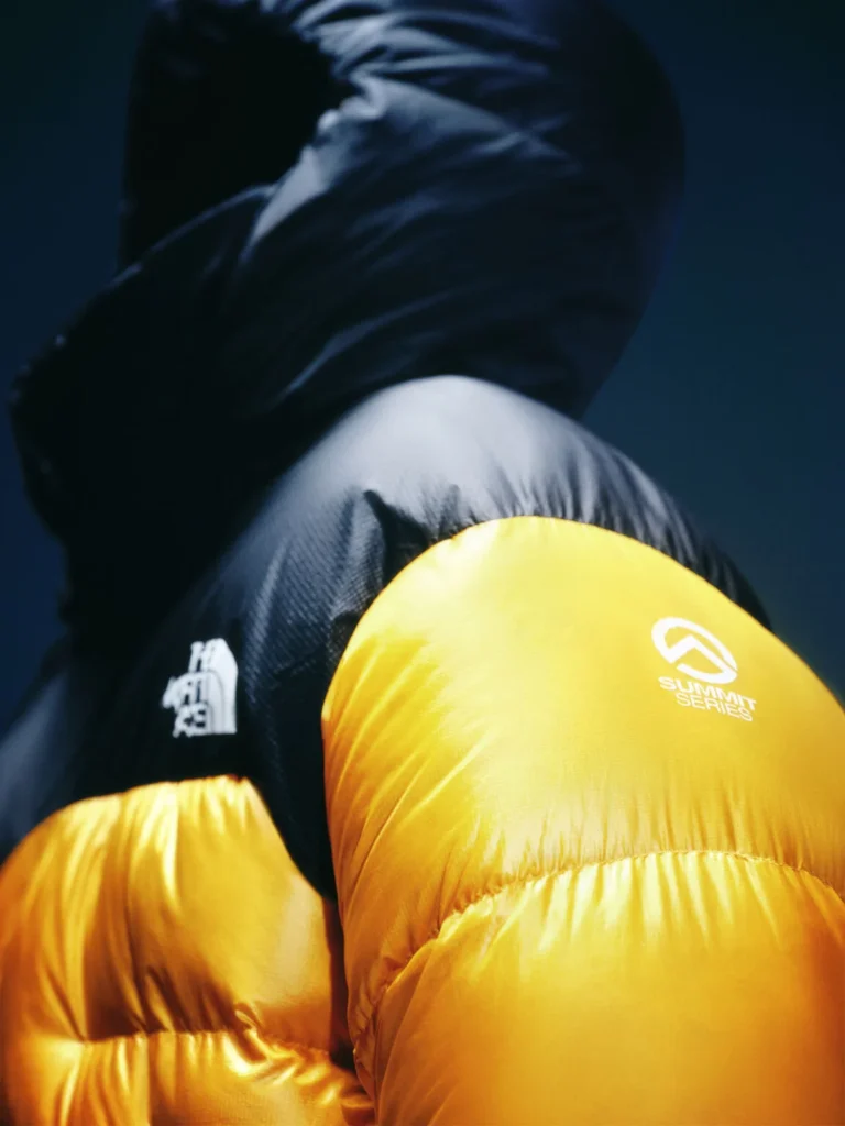 Close-up of a person in a black puffer jacket with bright yellow Summit Series sleeves against a dark blue background