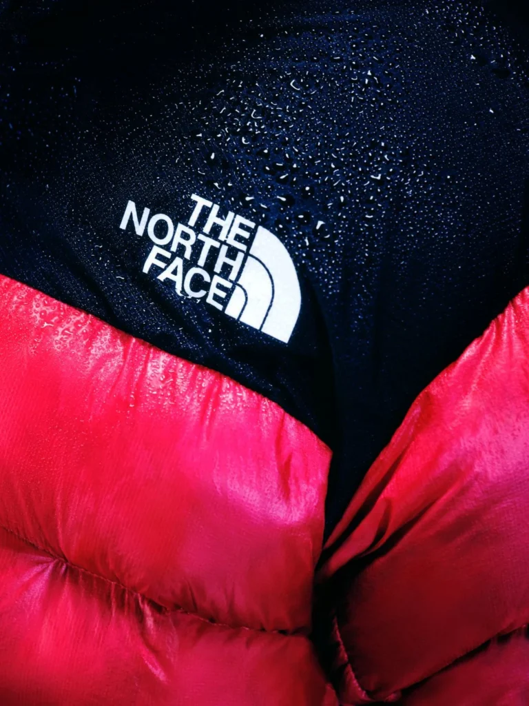 Close-up of a red puffer jacket and black hood with The North Face logo, covered in water droplets