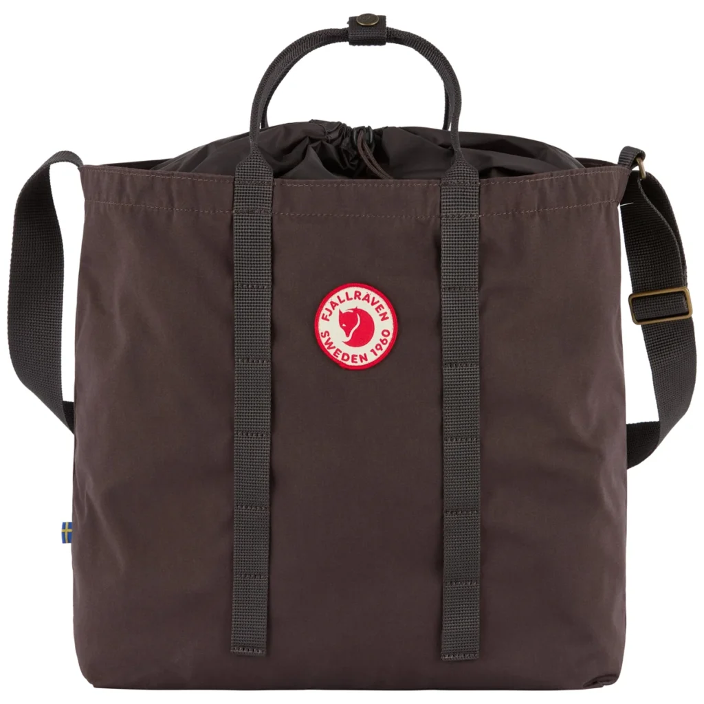Brown Fjällräven tote bag with black handles, shoulder strap, drawstring closure and red logo patch on white background