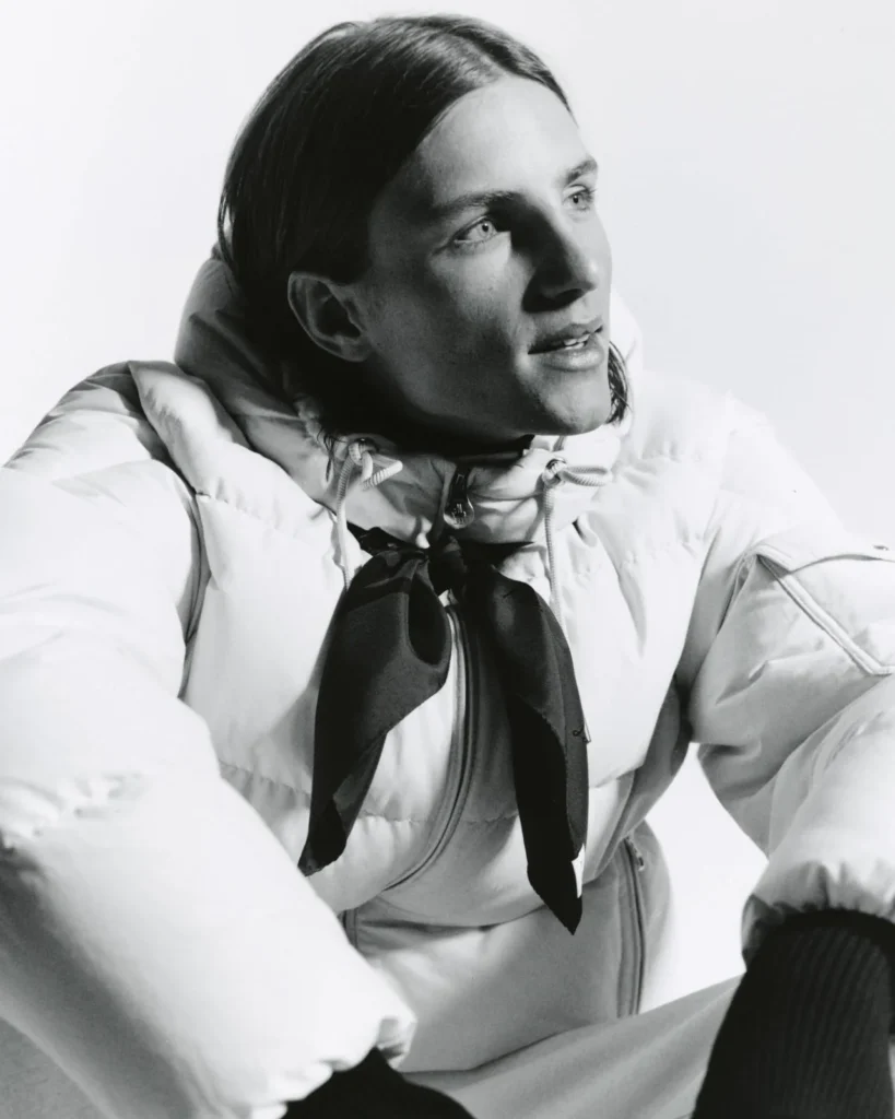 Black-and-white portrait of a person wearing a white puffer jacket and dark neck scarf