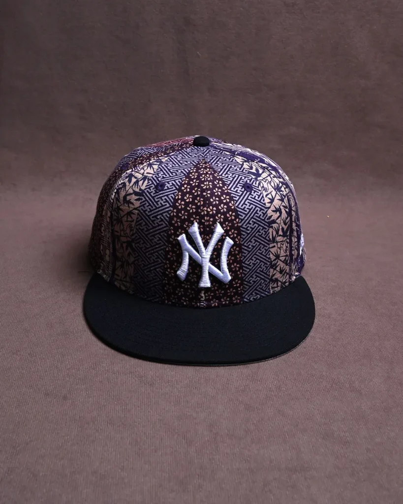Black-brimmed snapback cap with a geometric patterned crown and white embroidered NY logo on brown fabric background
