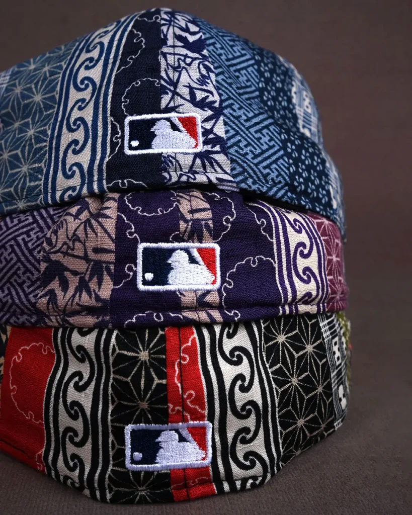 Three stacked baseball caps with MLB logos, featuring dark patterned fabric in blue, beige, black, white and red