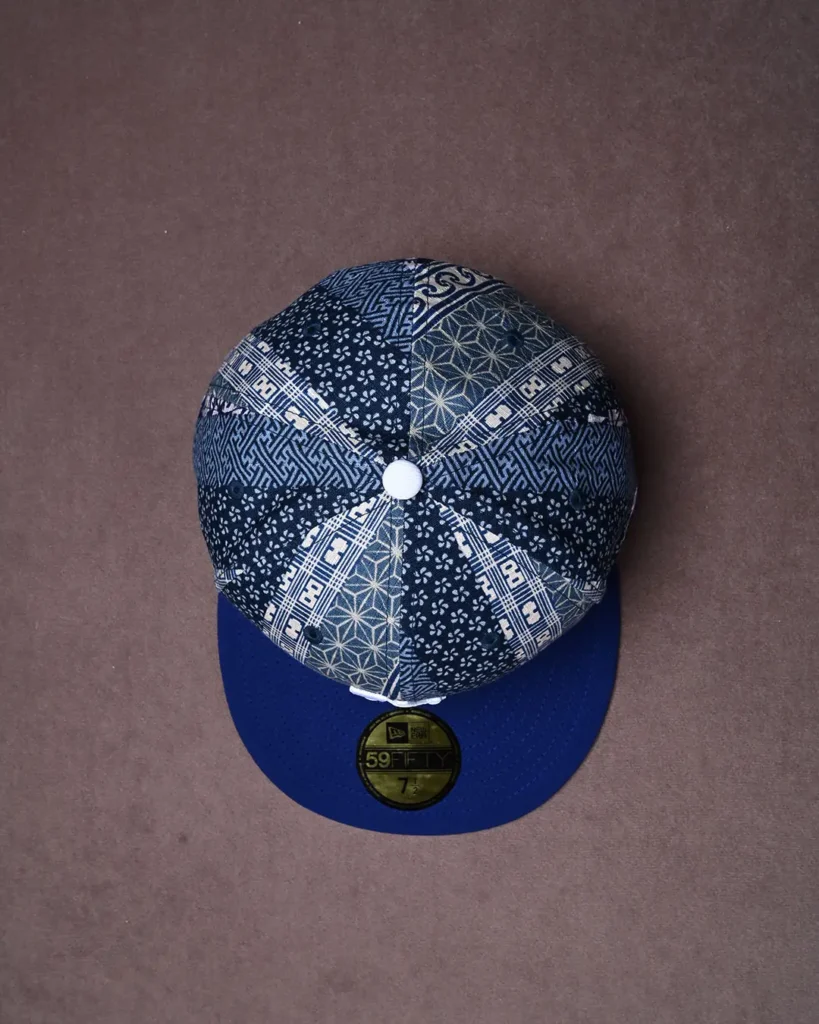 Patchwork-patterned blue baseball cap with a white button and curved brim on a brown background