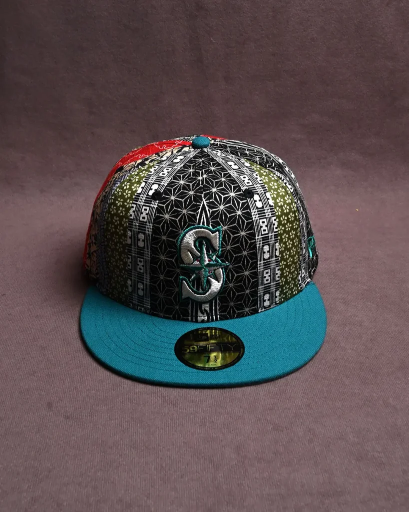 Black patterned baseball cap with a teal brim and raised teal-and-silver letter S on the front