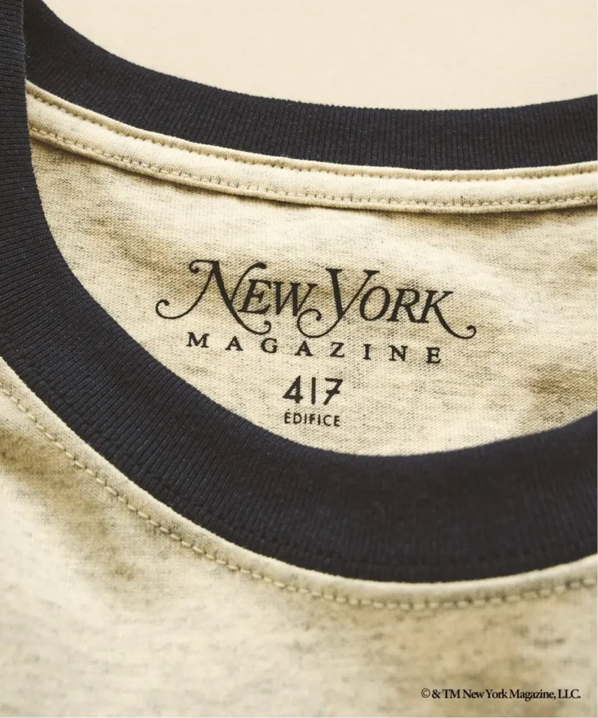 Close-up of a cream T-shirt collar with black ribbing and printed New York Magazine 417 Edifice label