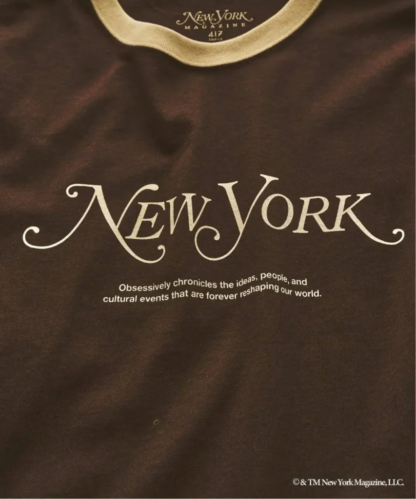 Close-up of a dark brown T-shirt with a cream ribbed collar and large cream New York Magazine logo text