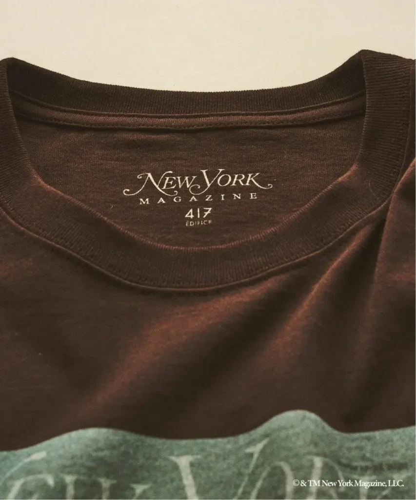 Close-up of a dark brown T-shirt collar labeled “New York Magazine 417 Edifice” over green patterned fabric