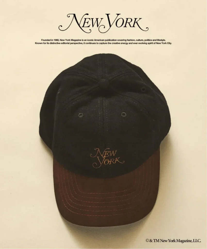 Black New York Magazine baseball cap with brown stitching, photographed against a cream background