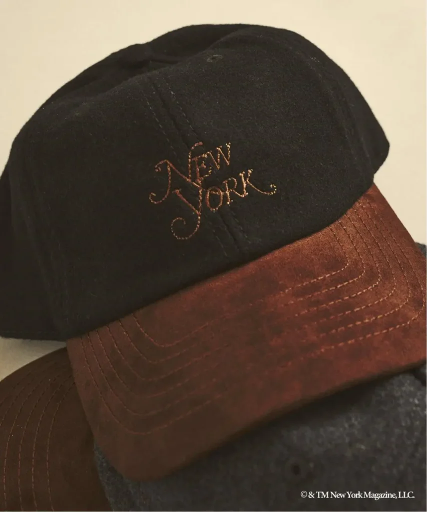 Close-up of a black cap with brown brim, embroidered New York text, and visible stitching against a neutral background
