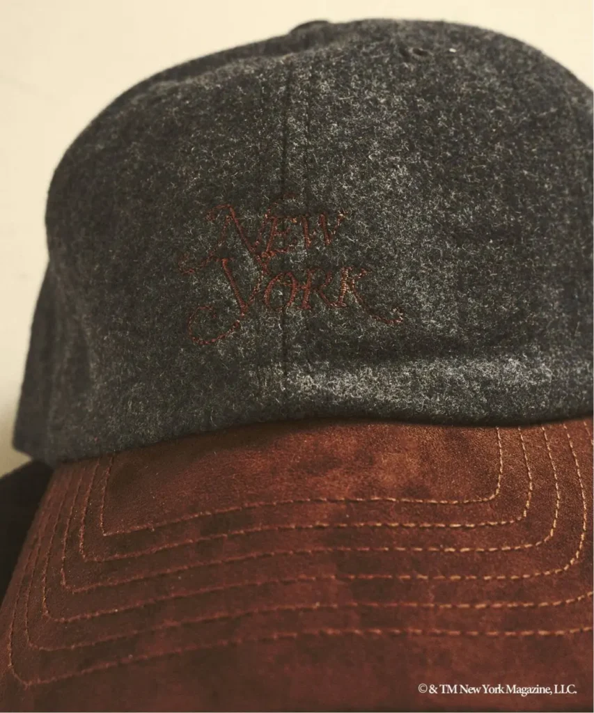 Close-up of a two-tone cap with a charcoal wool crown, brown leather brim, and red embroidered lettering