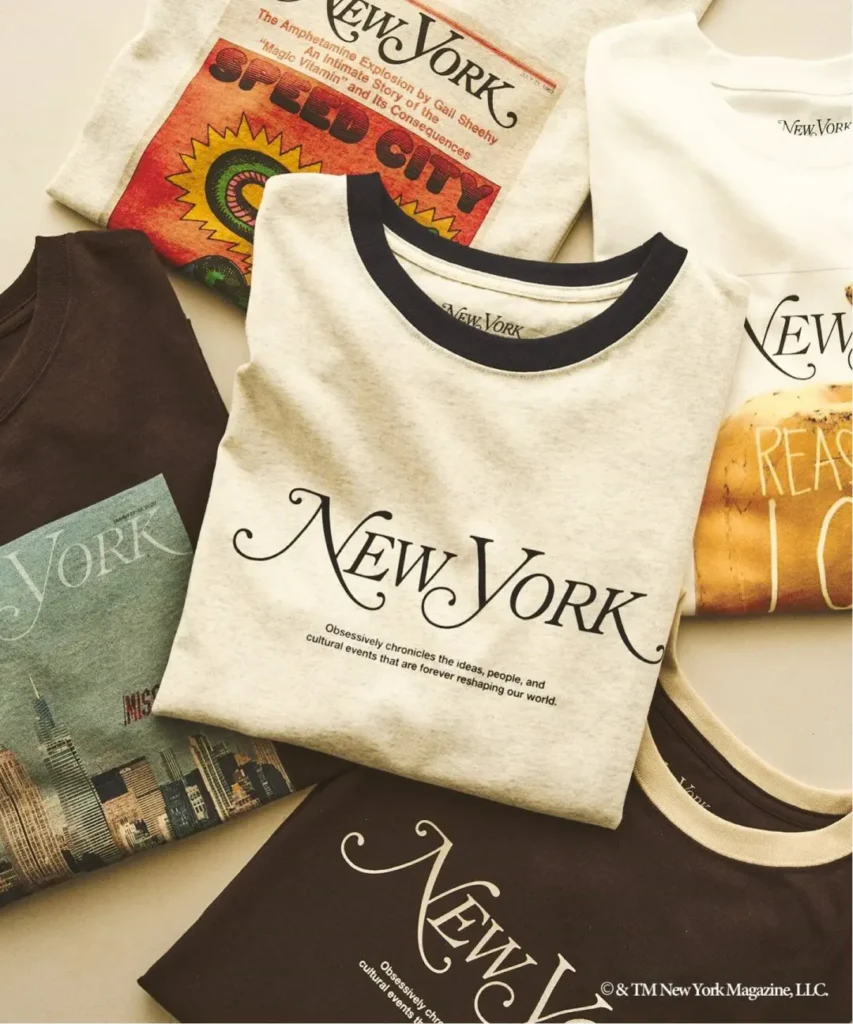 Flat lay of New York-branded T-shirts and magazines, including cream, black, and graphic designs on a light surface