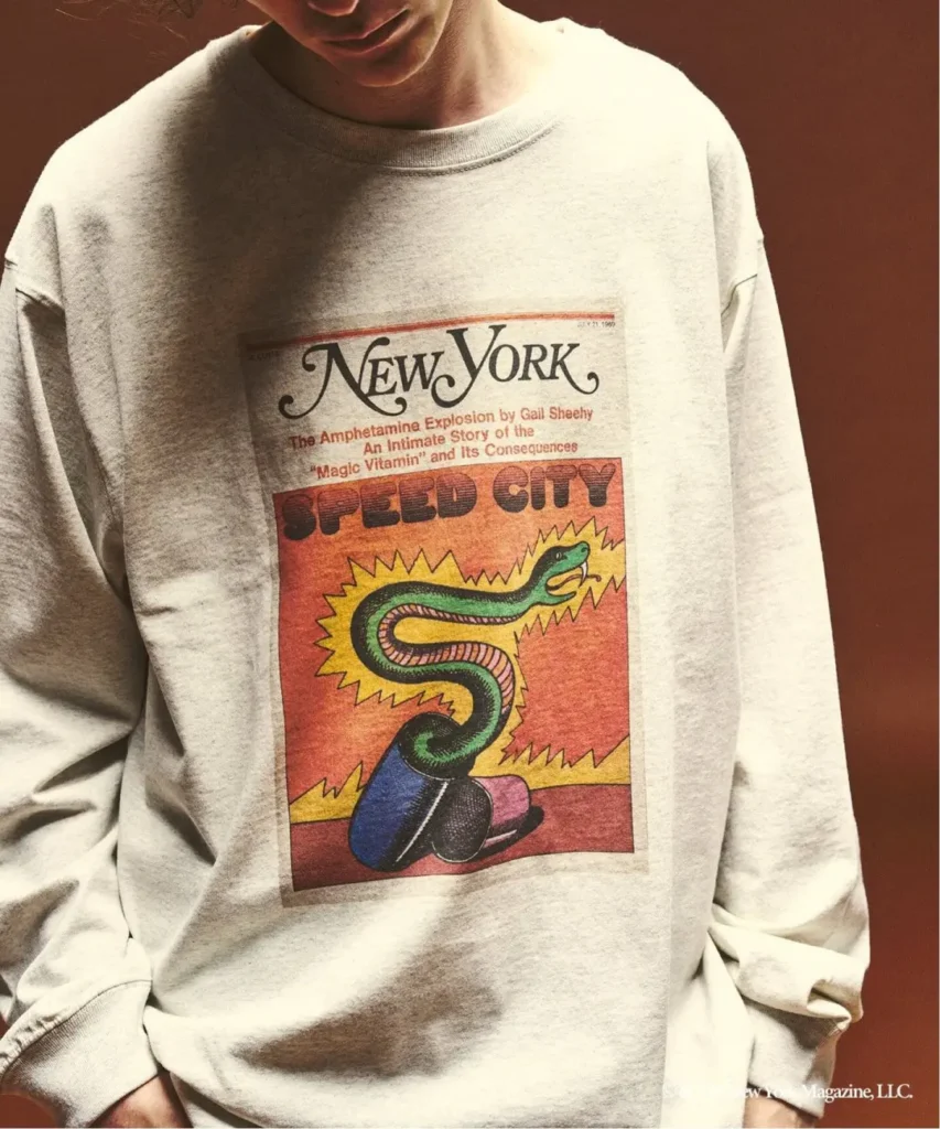Cropped person wearing a cream sweatshirt printed with a vintage New York magazine “Speed City” snake graphic against a