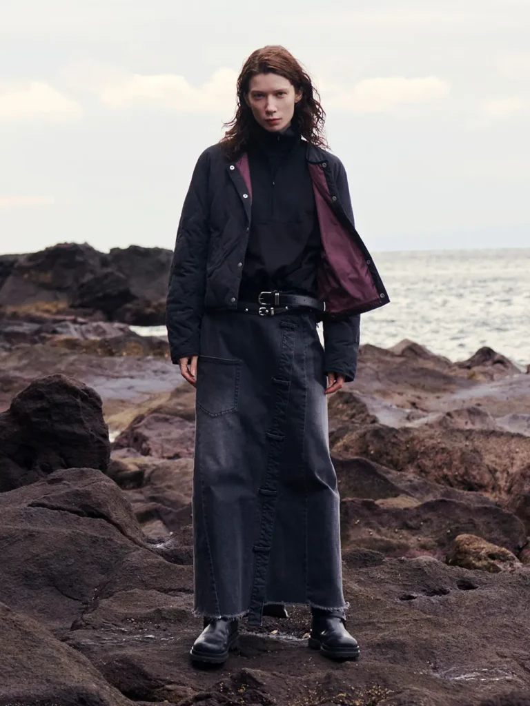 Person in dark clothing standing on rocky shore with the ocean behind them