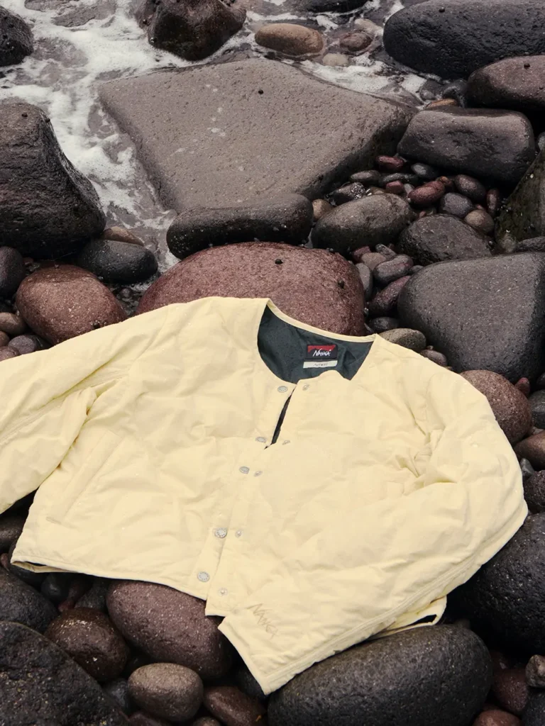 Pale yellow button-up shirt spread across dark, rounded rocks beside foamy seawater