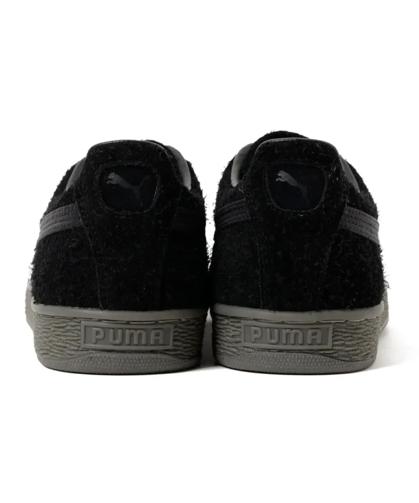 Rear view of black Puma sneakers with fuzzy uppers, gray stripes, and textured gray soles against a white background
