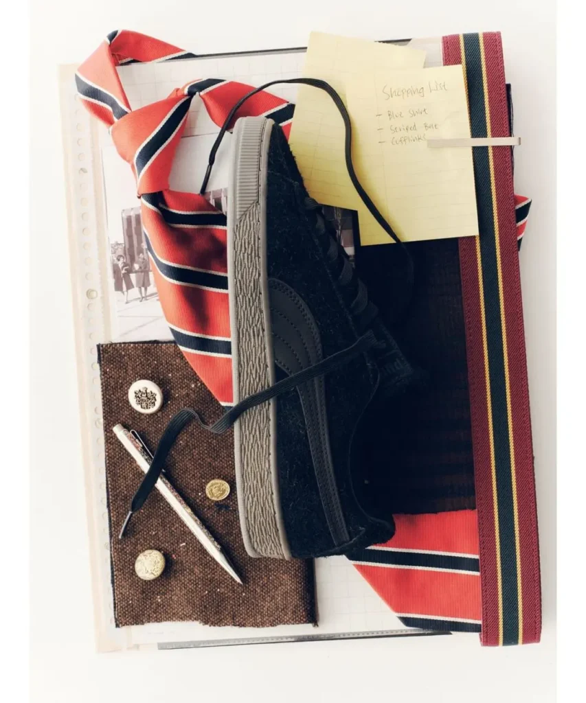 Top-down arrangement of a striped red tie, black sneaker, notebooks, handwritten shopping list, fabric swatches and ruler
