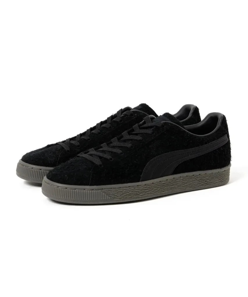 Pair of black fuzzy low-top sneakers with black laces, side stripes and gray textured rubber soles on a white background