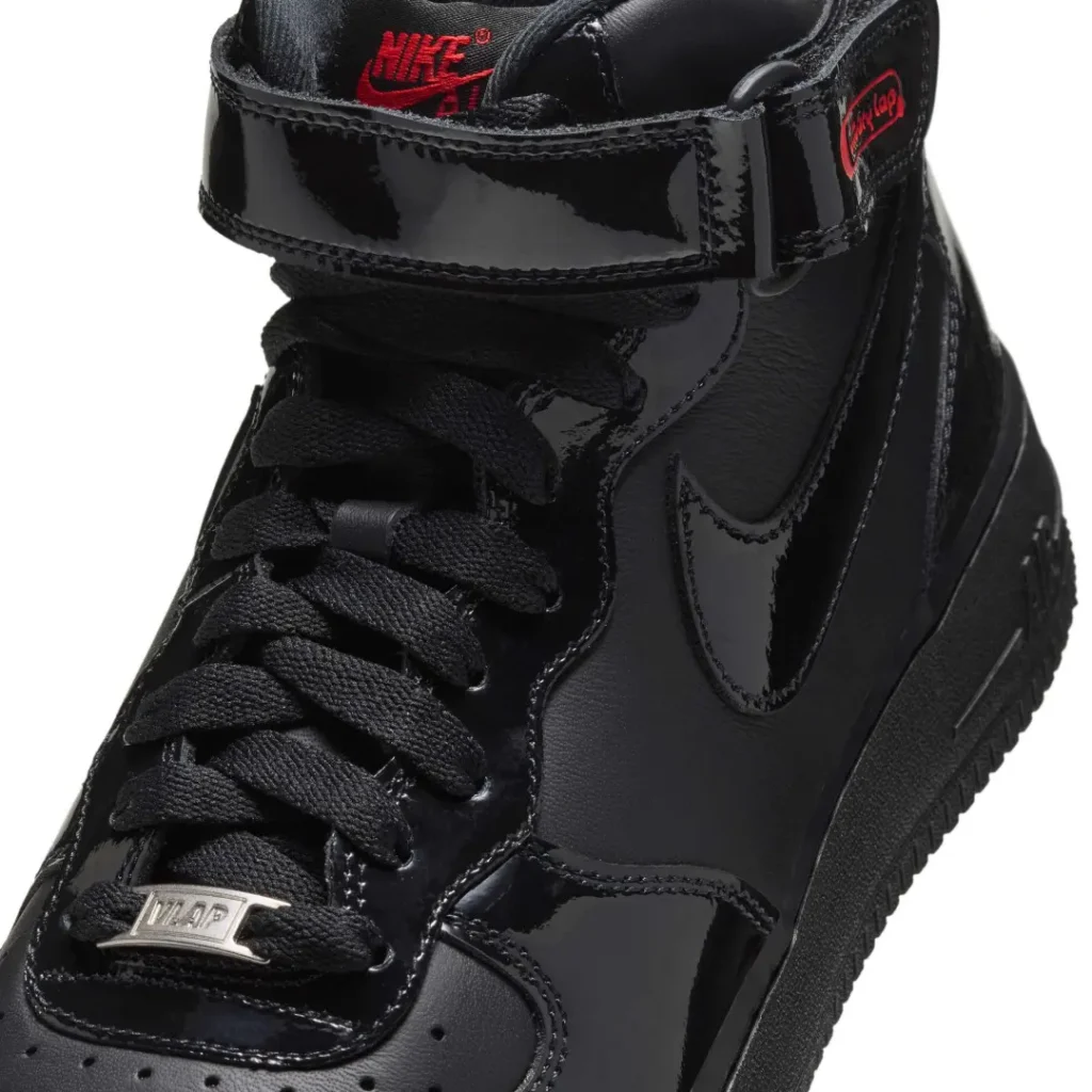 Close-up of a black patent Nike Air Force 1 Mid sneaker with black laces, ankle strap and red Victory Lap branding on white