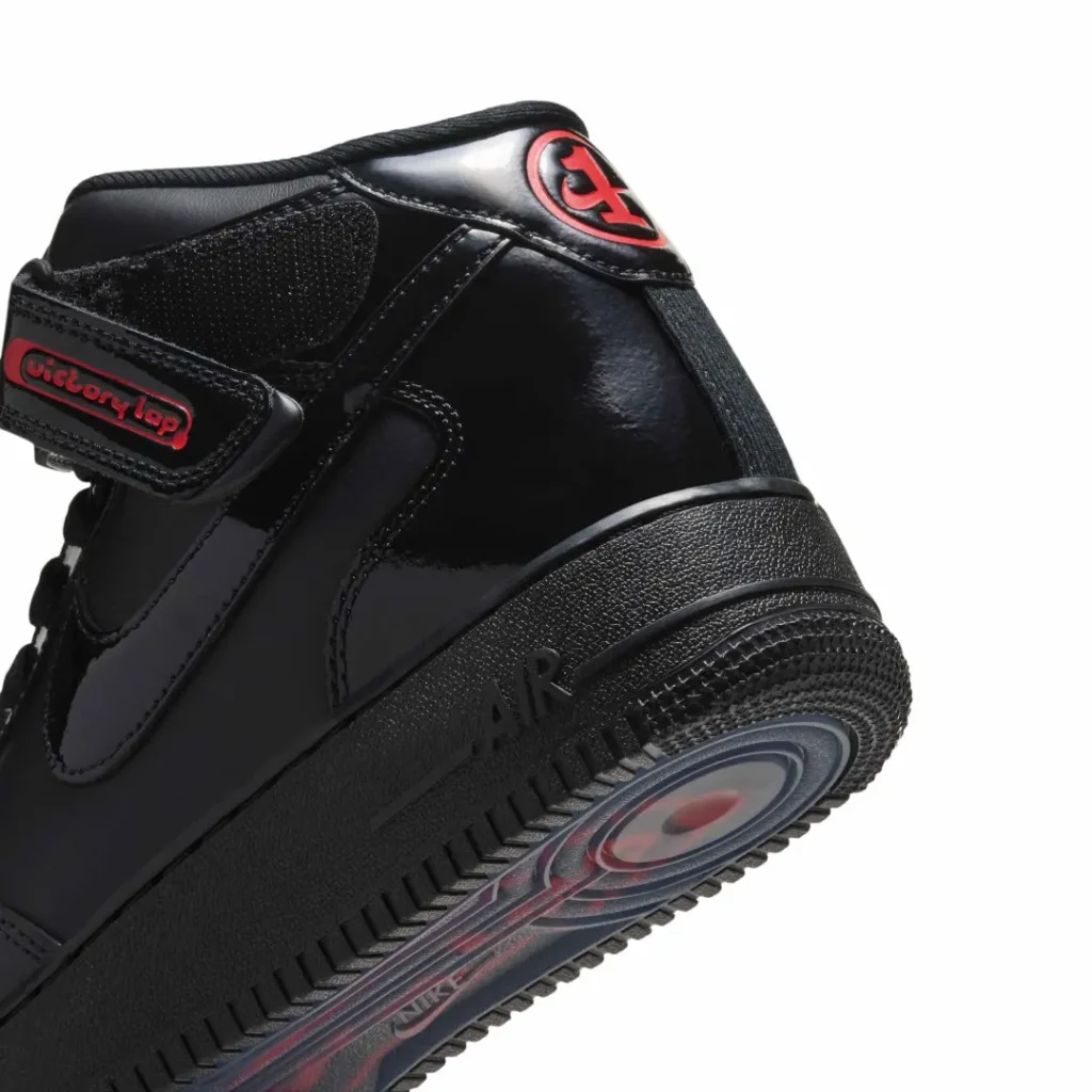 Close-up of a black patent Nike Air Force 1 Mid with red Victory Lap branding on the strap and tongue against white