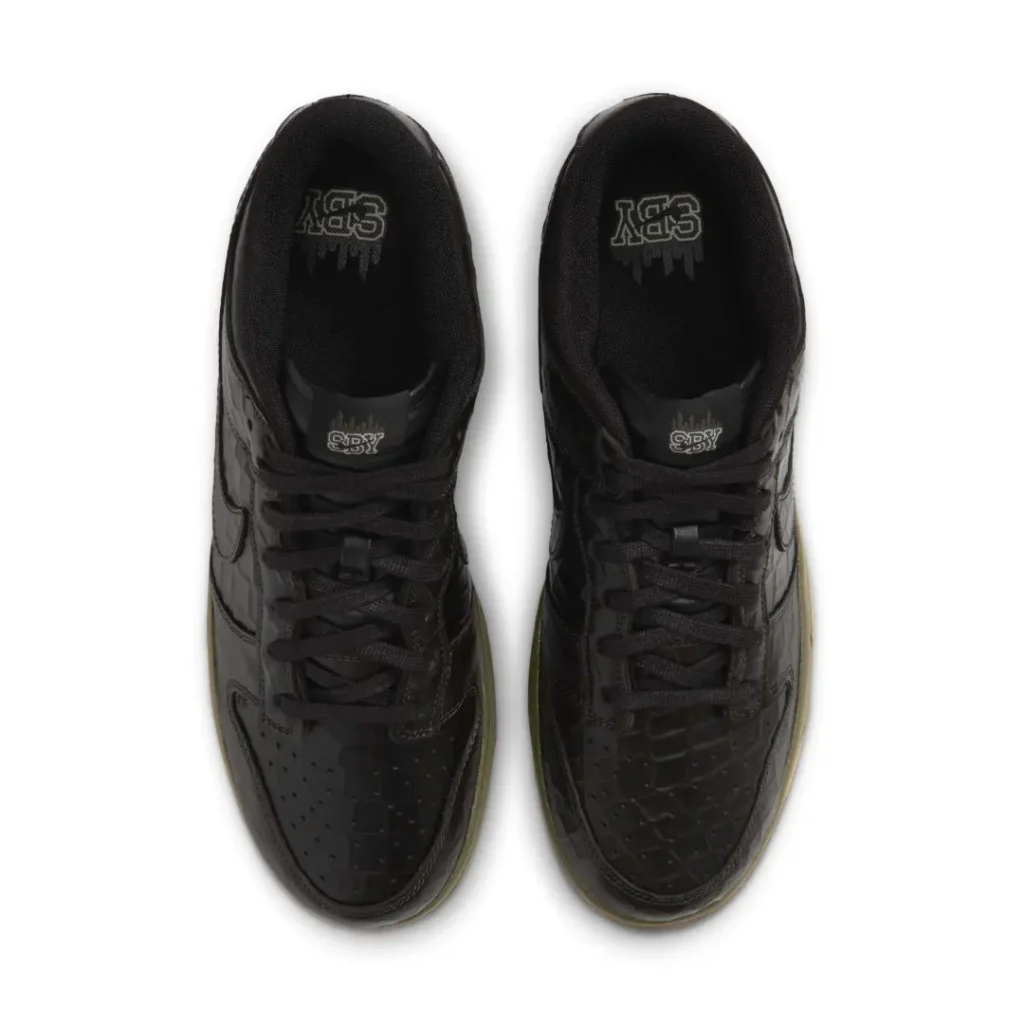 Pair of black low-top sneakers with textured panels, black laces, and translucent olive-green soles on a white background