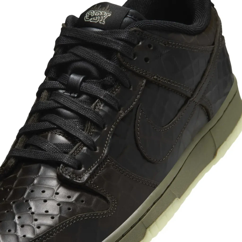 Close-up of a black Nike high-top sneaker with textured panels, black laces, and an olive translucent sole on white