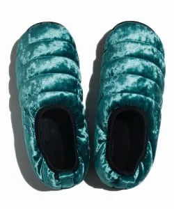 Pair of teal quilted slip-on shoes with black oval openings, viewed from above on a white background