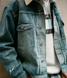 Close-up of a person wearing a blue denim jacket over a white shirt with black-and-light-blue graphics and a lightning patch