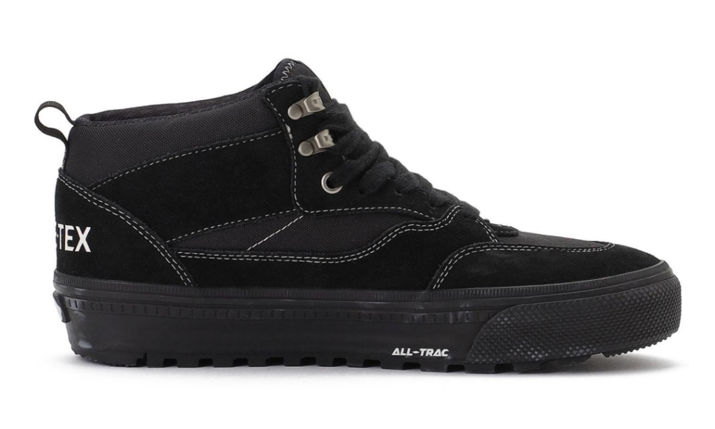 Black high-top shoe with white stitching, metal eyelets, textured toe, and thick lugged sole on a white background