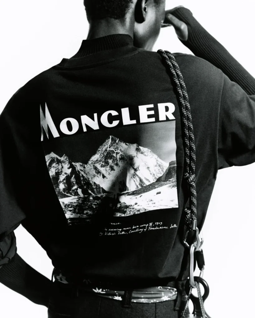 Back view of a person in a black Moncler sweatshirt with a mountain graphic, crossbody strap and metal carabiner against