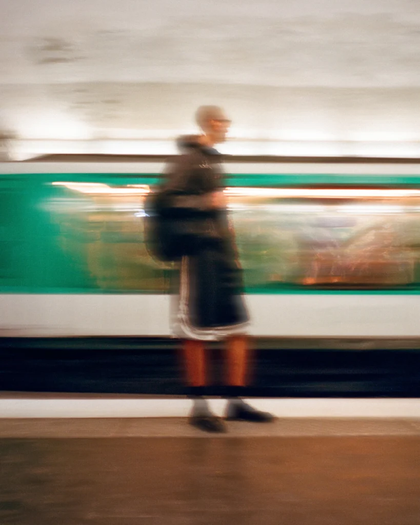 Motion-blurred person walking beside a green and white train in a subway station