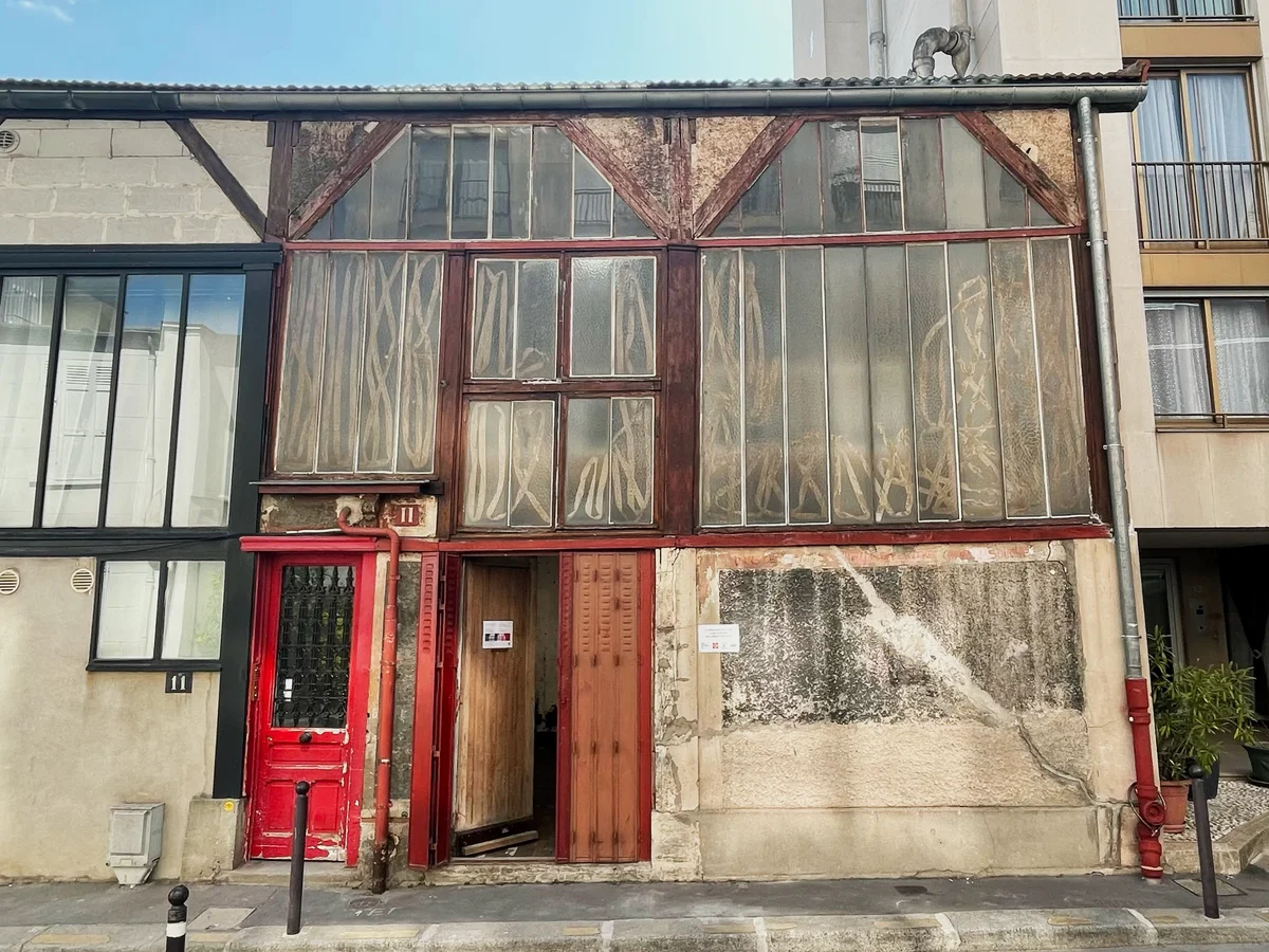 Weathered Parisian building facade with red doors, timber-framed windows, exposed pipes, and neighboring apartments