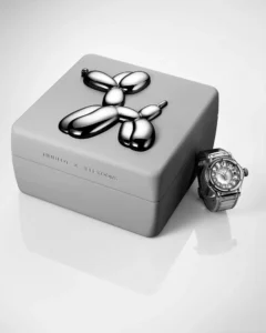 Silver Hublot watch beside a gray box labeled Hublot x Jeff Koons, topped with a metallic balloon-dog sculpture