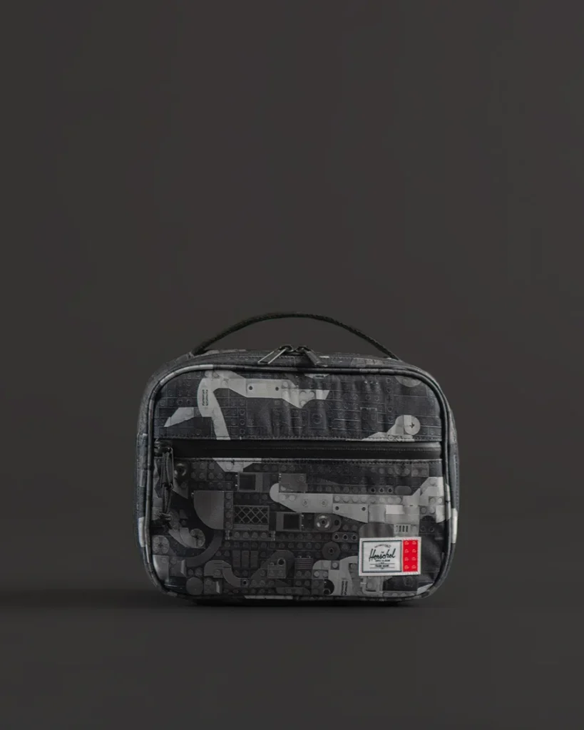 Gray patterned zippered toiletry bag with top handle, displayed against a dark background