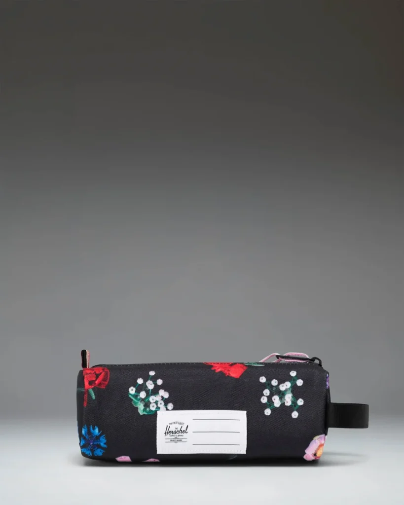 Black floral Herschel pouch with a white label, pink zipper pull, and side handle on a gray background