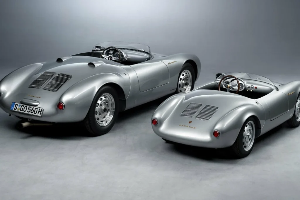 Two silver Porsche 550-style roadsters with open cockpits and wire wheels displayed on a gray studio floor