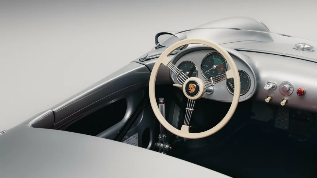 Close-up of a silver roadster cockpit with an ivory three-spoke steering wheel, analog gauges, and red dashboard button