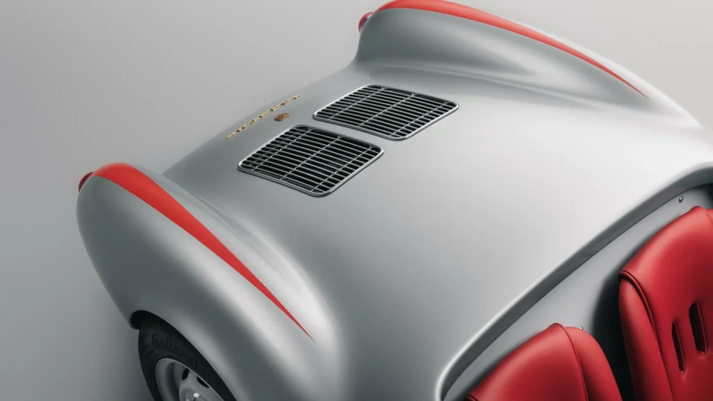 Close-up of a silver sports car rear with twin black grilles, red trim, red seats, and a gold Porsche badge