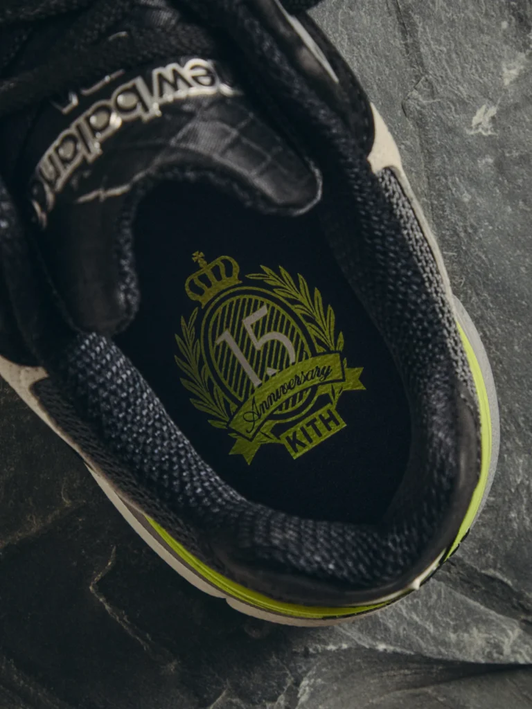 Close-up of a black shoe with neon yellow trim, textured panels and a gold anniversary crest on the insole