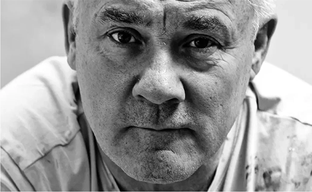 Black-and-white close-up portrait of an older gray-haired man in a light shirt, looking directly at the camera