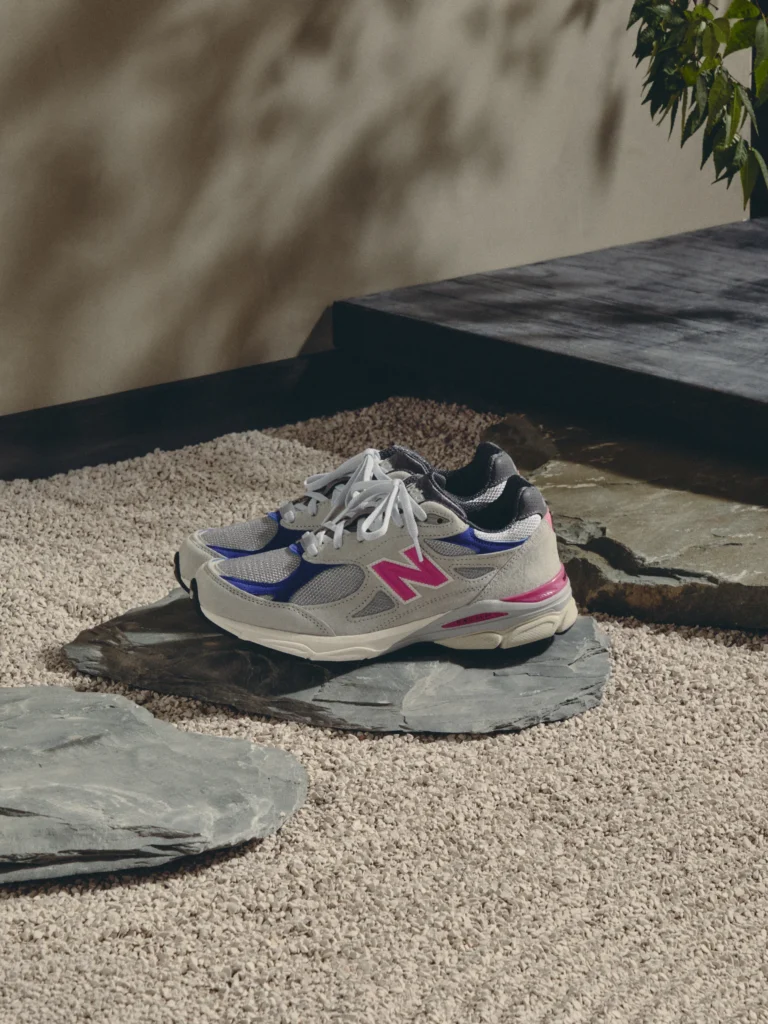 Pair of gray mesh sneakers with blue and pink accents on slate stepping stones over white gravel outdoors