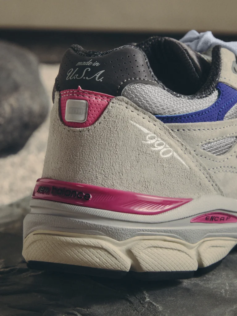 Close-up of a beige, pink and blue New Balance sneaker with suede panels, perforations and “made in U.S.A.” tongue text, on