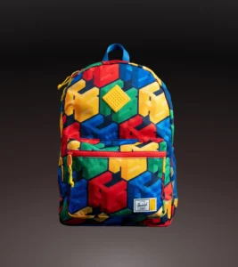 Tincture backpack with a raised yellow brick patch, patterned with red, blue, green and yellow interlocking blocks against a